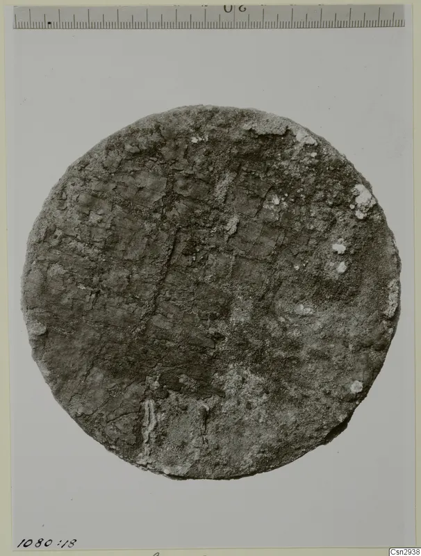 Flat circular object with a grid pattern of square impressions on its encrusted surface.