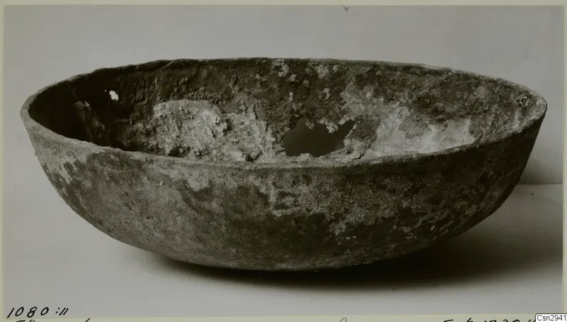 Bowl before conservation, with a crusty encrusted surface and a broken hole in the inner wall.