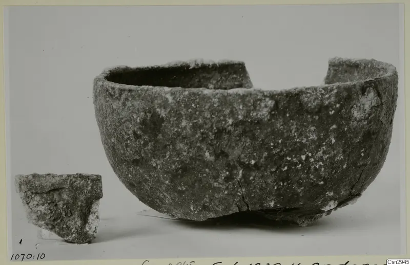 A large rough-surfaced bowl with a broken rim and a separate sherd beside it