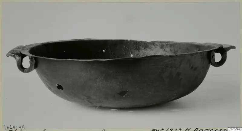 Dark metal bowl with a wide flaring rim and two loop handles, photographed on a pale background