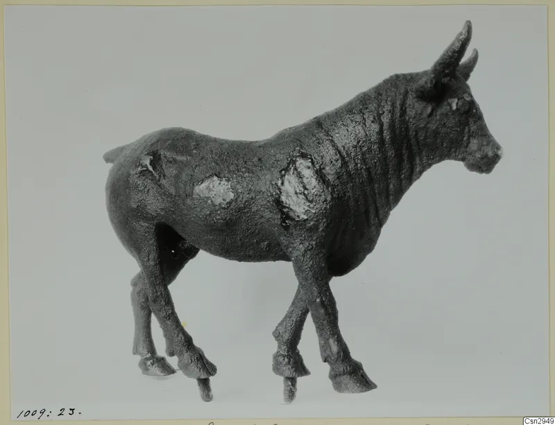 Small standing animal figure with two horns and a crusted dark surface, photographed before conservation