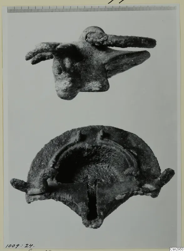 Two corroded metal objects: a small figure with a long projection above a curved, hollow object below