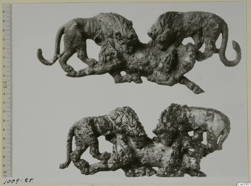 Two corroded openwork metal figures, each showing two maned cat-like animals with curled tails, shown one above the other