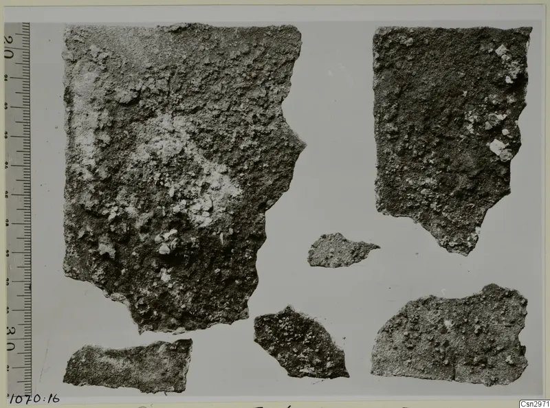 Six broken sherds with rough, crusted surfaces laid out beside a measuring scale.