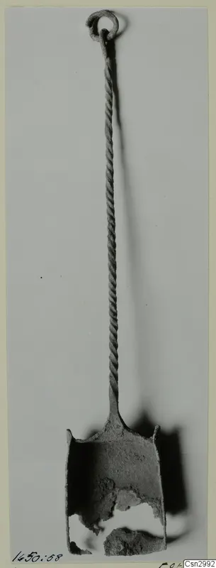 Corroded metal object with a ring at the top, a long twisted shank and a broken cup-shaped end, before conservation