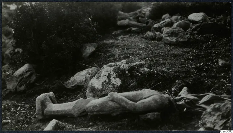Carved stone fragment of a figure lying on grass among rocks and scrub on the Karpas peninsula