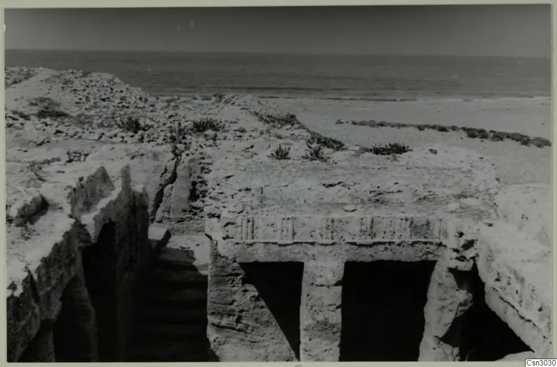 Excavated rock-cut structure with two doorways and a stepped passage, with the sea beyond