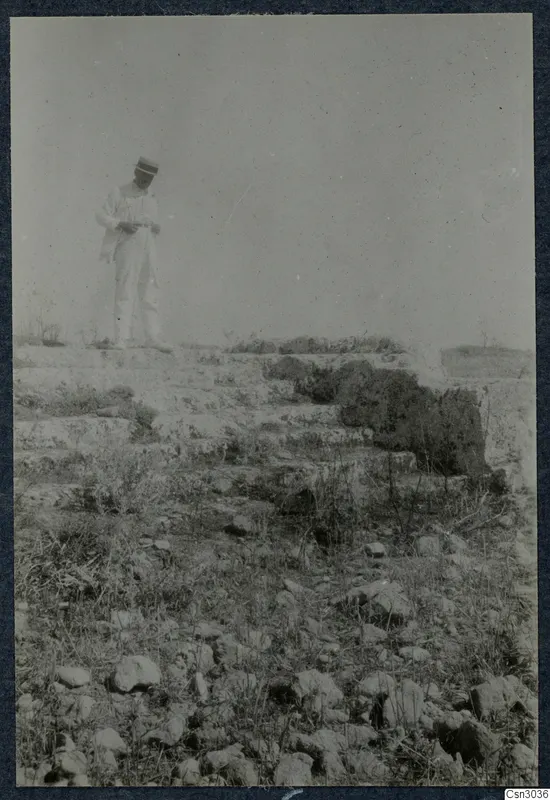 Man in a light suit and hat standing on a stepped stone ledge among scattered stones at Paphos