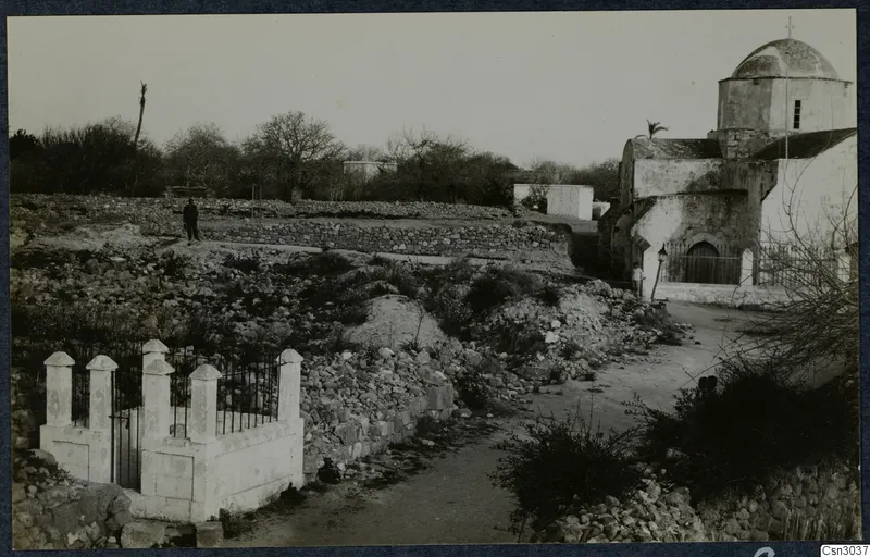 Stone walls, a whitewashed domed church and a figure beside a dirt path at Paphos
