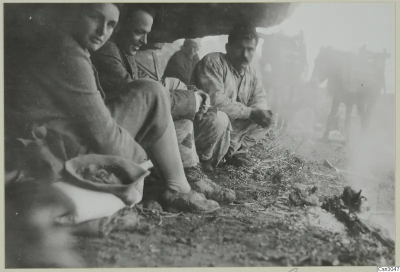 Four people sitting under a rock overhang, with two laden donkeys standing in the haze behind them