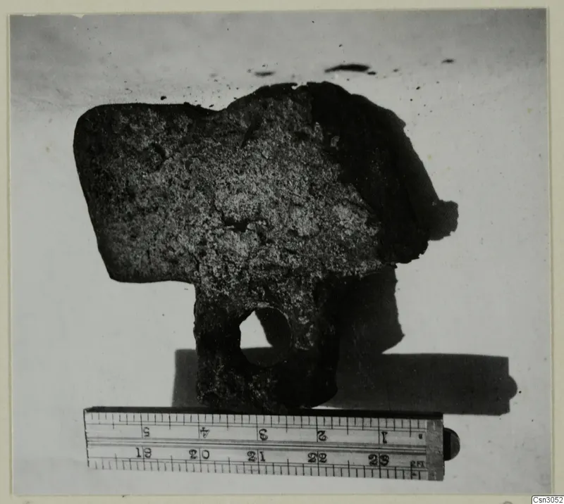 Corroded iron hoe with a round hole in its blade, shown beside a ruler.