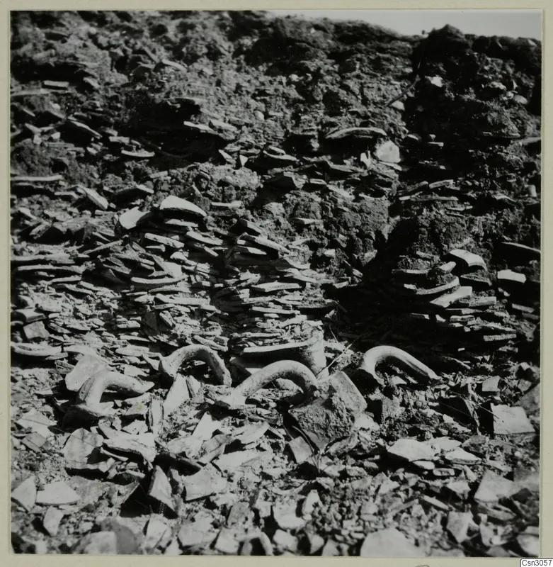 Curved tubular pieces and flat broken fragments lying among soil, shown as parts and objects from copper mining