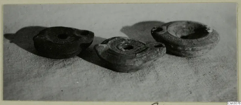 Three small lamps with nozzles and central filling holes resting on a textured cloth