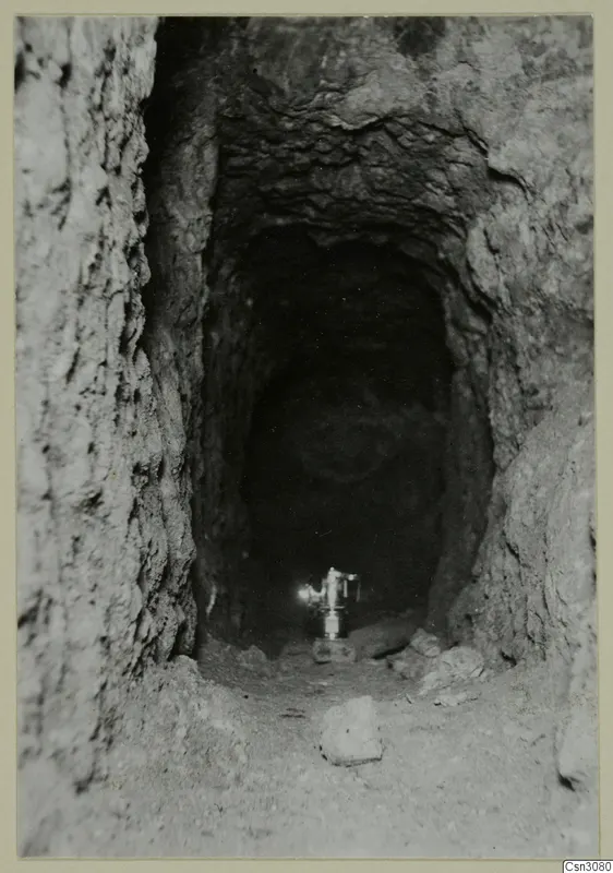 Narrow rock-cut gallery at Mavrovouni, with a lamp standing on the floor at its far end.