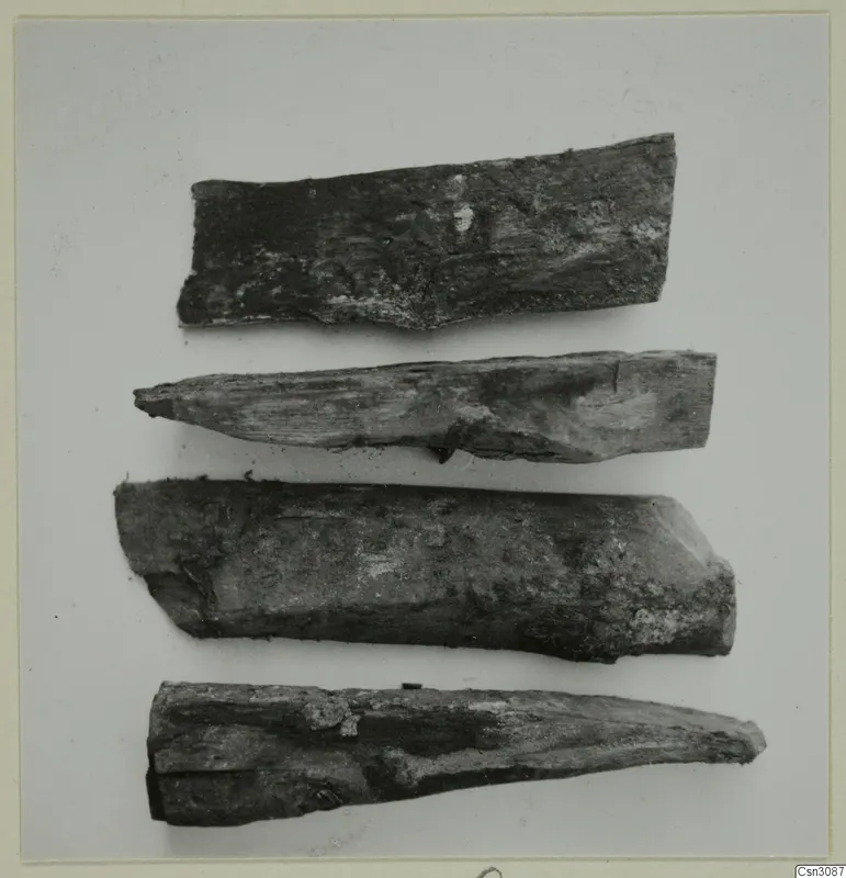 Four ancient wooden wedges lying in a row on a pale background.