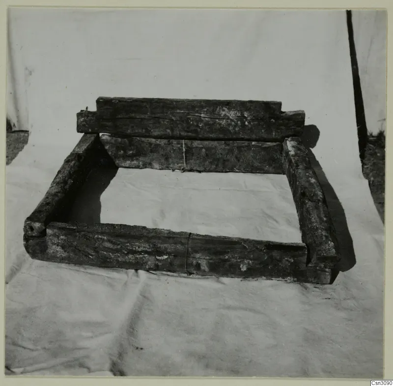Ancient wooden crib-timbers forming a frame, set on a light cloth in front of a tent.