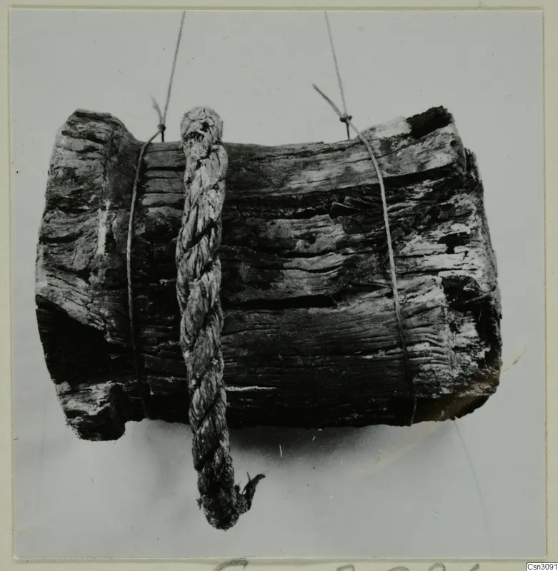 Weathered wooden cylinder with a braided rope hanging across it, tied with thin cords against a plain grey background