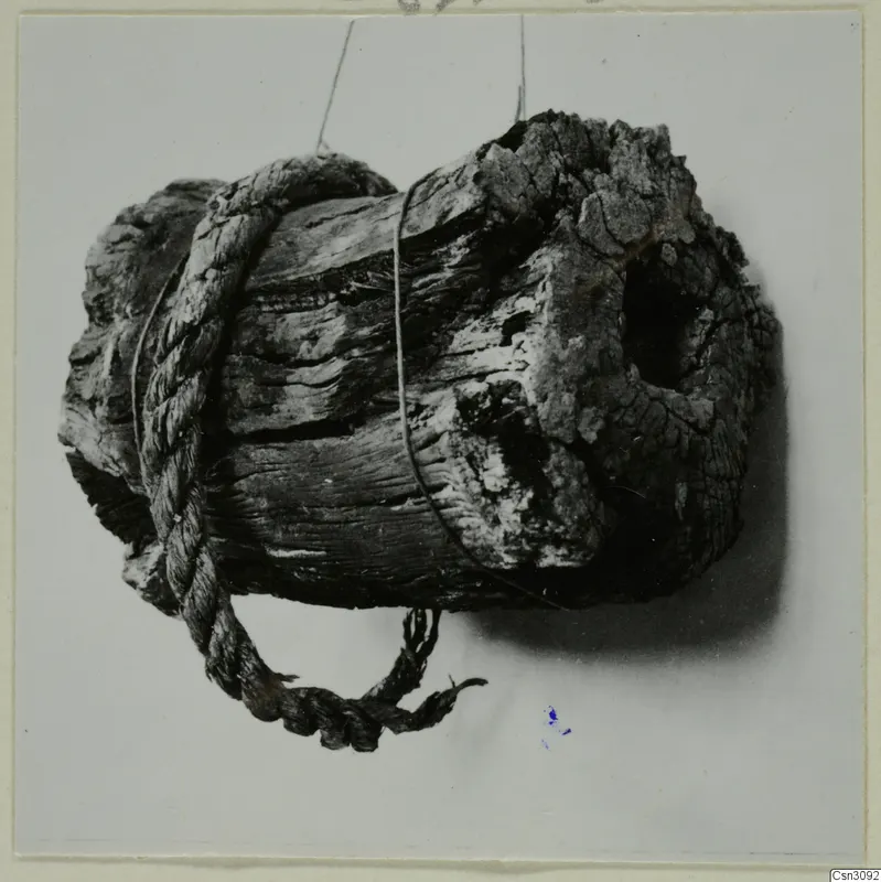 Rope wrapped around a weathered wooden object, a mining find photographed against a pale background
