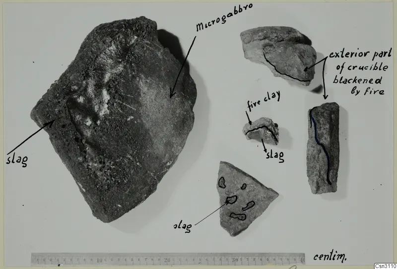 Fragments of stone and fired clay with handwritten labels and a centimetre ruler along the bottom edge.