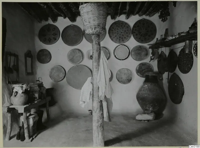 Interior of a room with round woven baskets hung on the walls and a large pottery jar on a stone base