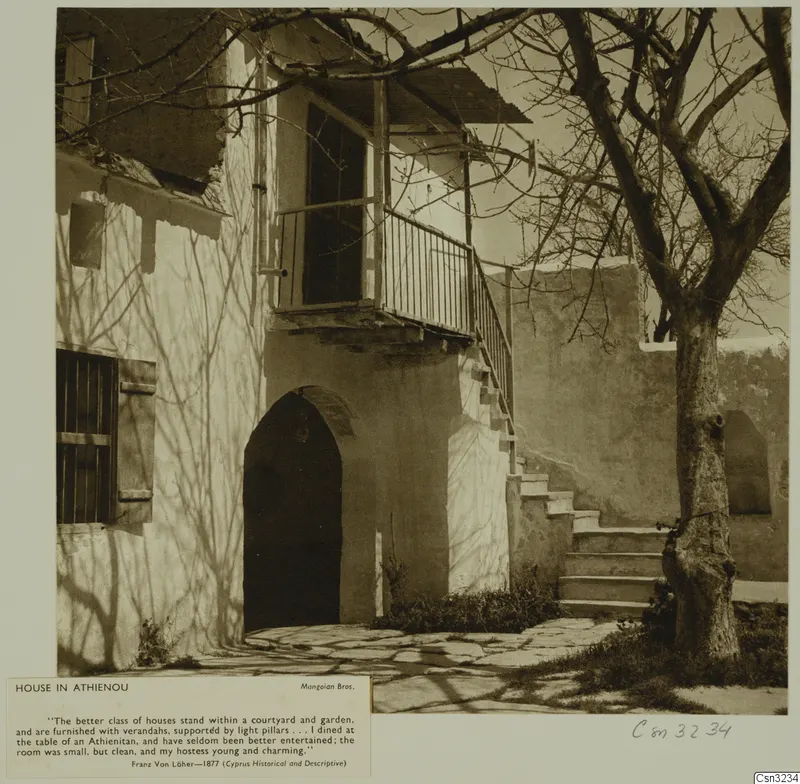 House in Athienou with an arched doorway, a wooden balcony and an outside flight of stone steps, beside a bare tree