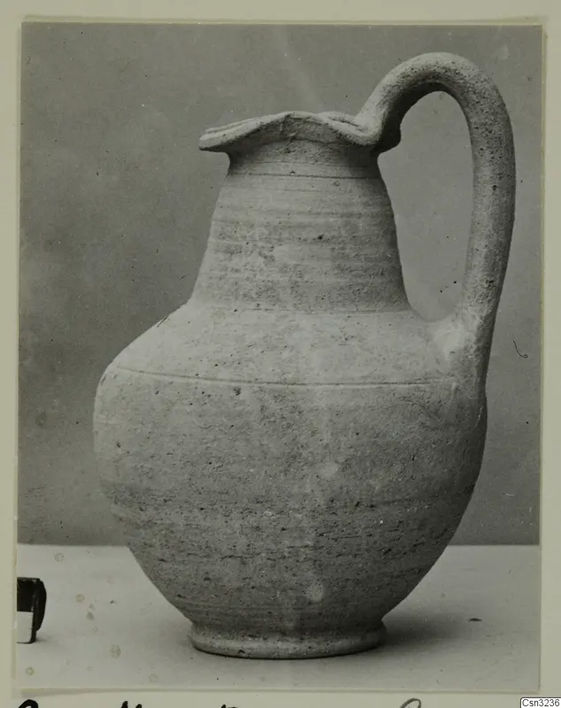 Plain pale pottery jug with a strap handle and flared, wavy rim, photographed on a light surface