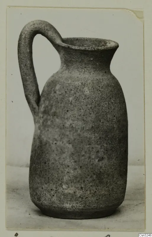 Plain pottery jug with a strap handle and wide mouth, photographed on a pale surface.