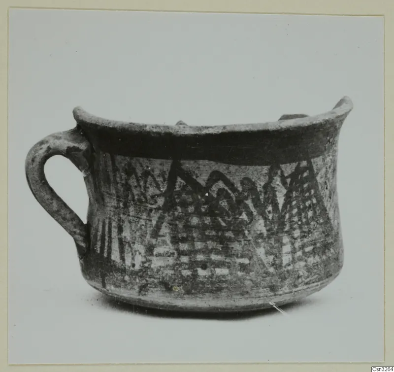 White Painted pottery cup with a loop handle, a dark band under the rim and zigzag and hatched bands on the body