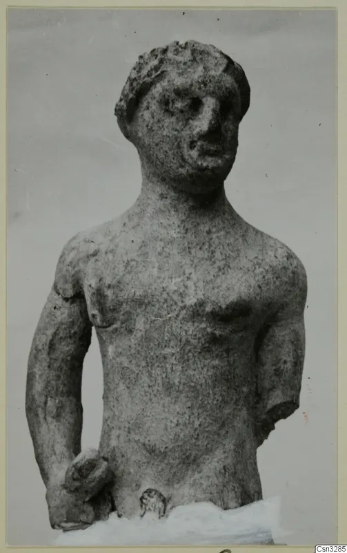 Terracotta figurine of a standing male figure with one arm broken off, shown against a plain grey background