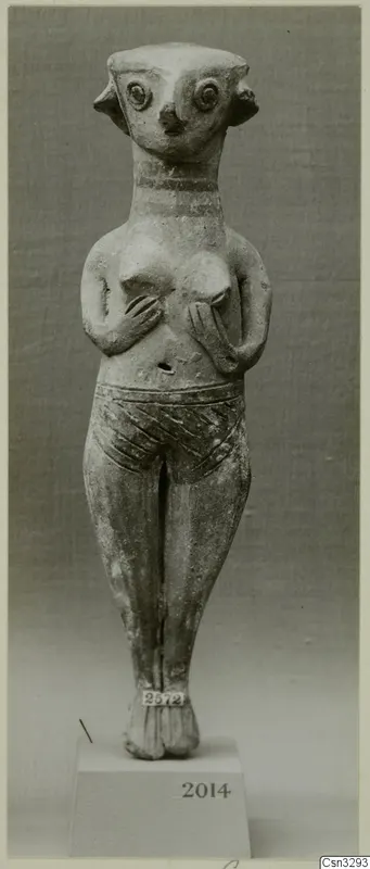 Standing terracotta figurine with large round eyes, a beak-like nose, hands on its chest and an incised belt