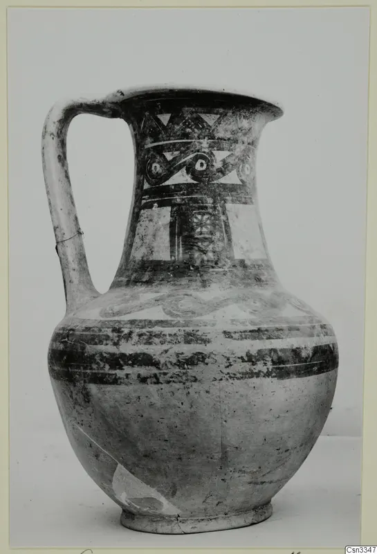 Painted pottery jug with a strap handle, decorated with bands, triangles and spiral motifs in dark paint on a light body.