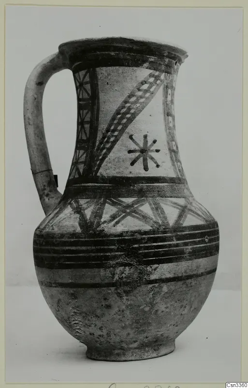 Painted jug with a strap handle, dark banded and cross-hatched decoration on a pale surface