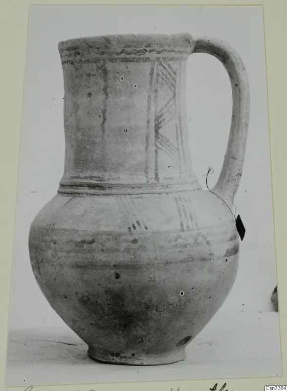 Wheel-made pottery jug with a single handle, painted bands and diagonal hatched strokes on the shoulder.