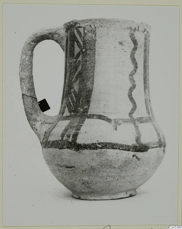 Wheel-made painted jug with a strap handle and dark painted bands, zigzag and vertical pattern on a pale body.