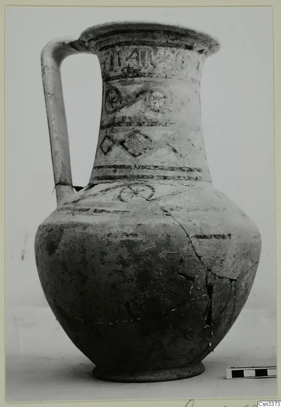 Wheel-made painted jug with a tall handle and banded decoration on the neck and body, shown against a plain background.