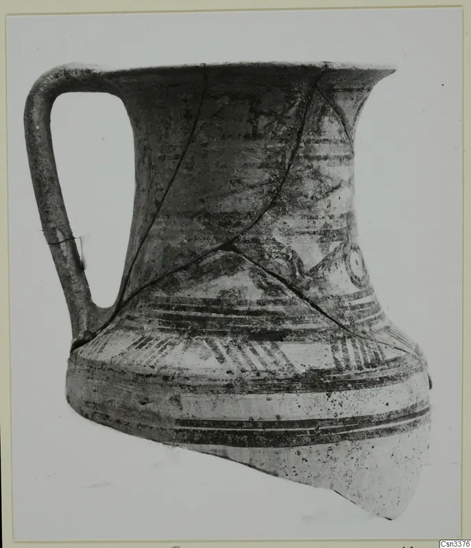 Wheel-made bichrome jug with a strap handle, shown on a card mount
