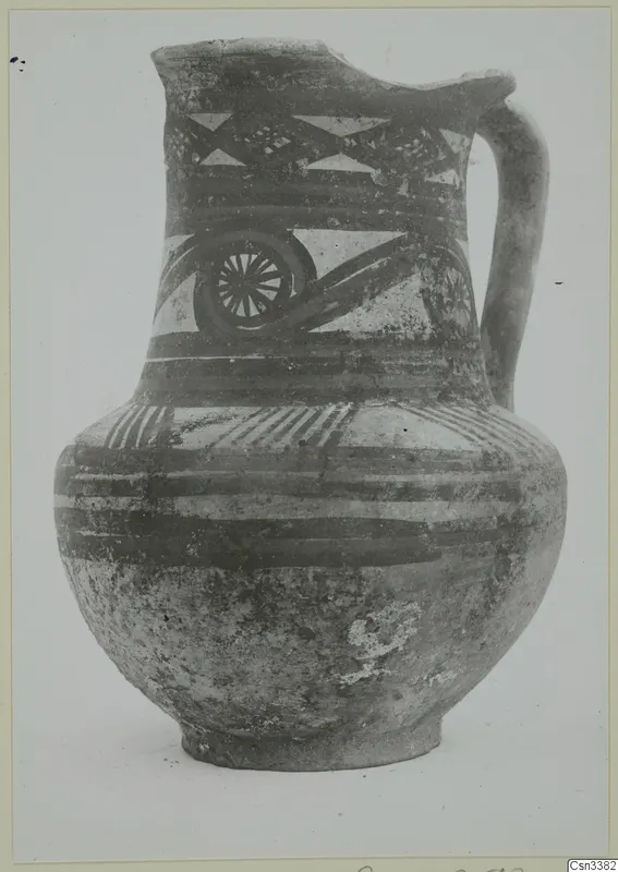 Painted pottery jug with a single loop handle, decorated with bands, triangles and a wheel-like motif.