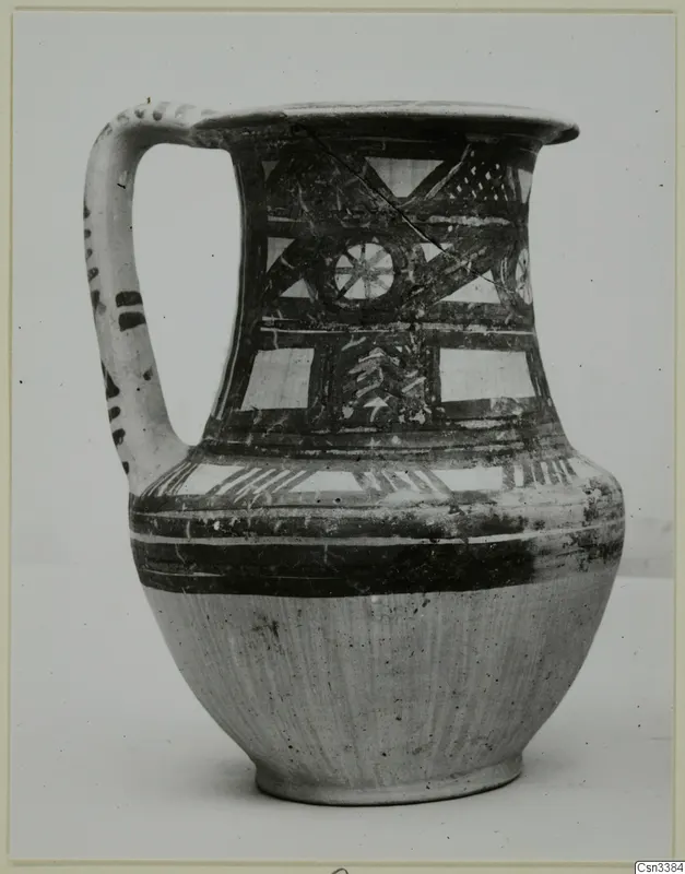 Painted wheel-made jug with a strap handle, dark geometric bands and a lattice panel on a pale ground.