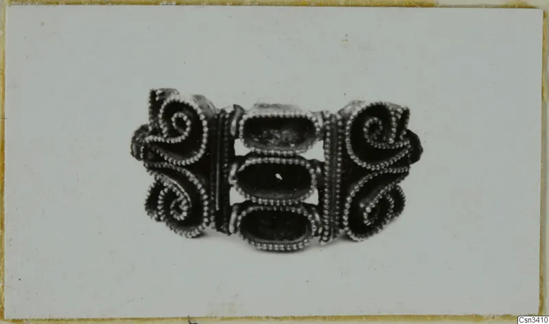 Gold jewellery piece with spiral scrolls and beaded wire edging, shown on a pale card