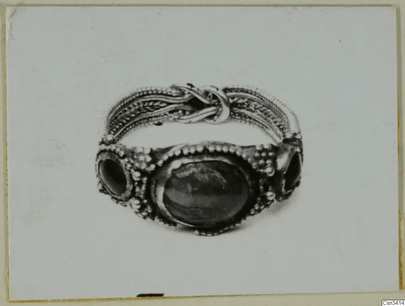 Ring of metal with twisted wire bands, a knot on top, and a dark oval stone flanked by two smaller stones