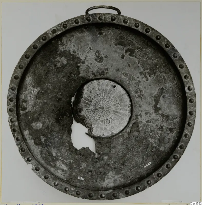 Round metal object with a studded rim, a loop handle and an engraved central boss