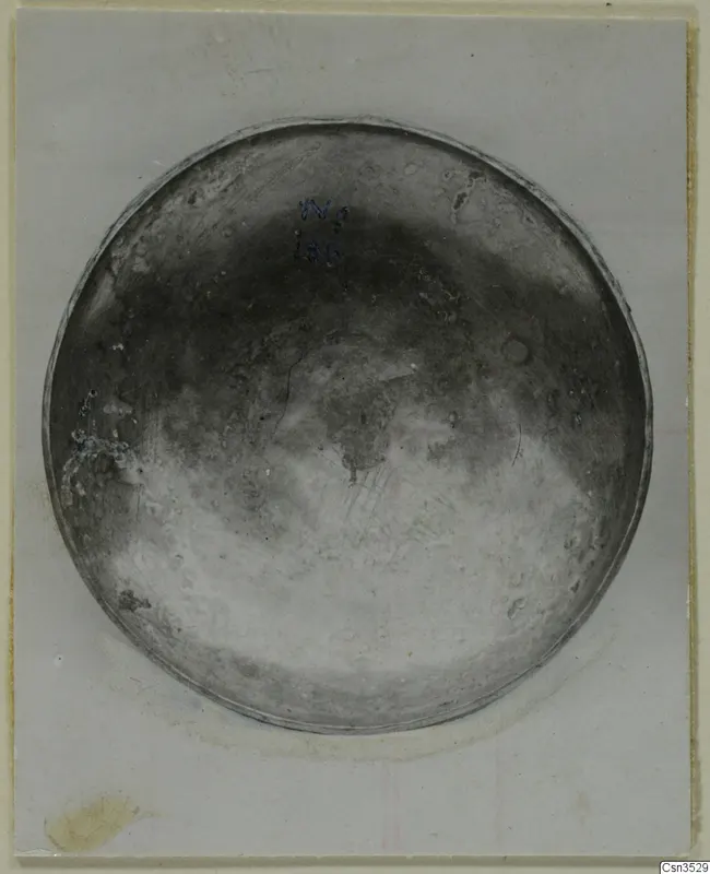 Shallow circular metal bowl seen from above, with a handwritten number label in blue ink on its inner surface