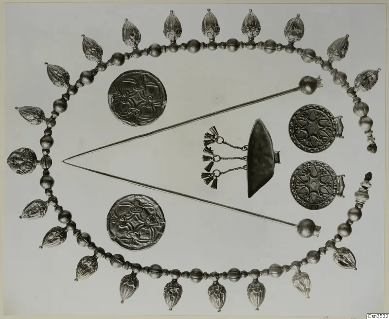Gold jewellery laid out flat: a beaded necklace with pendants, two long pins and several discs.