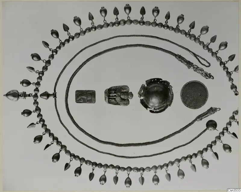 Gold jewellery laid out on a pale background: a bead and pendant necklace, two chains, a relief plaque, a broken bowl and a mesh disc
