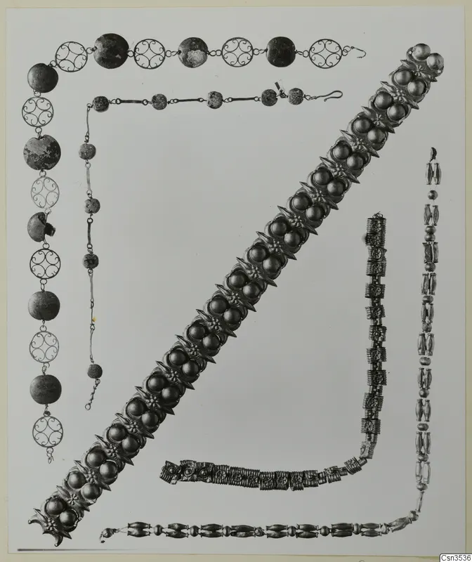 Several necklaces and a wide bracelet of metal beads, filigree discs and rosette ornaments, laid out on a pale background.