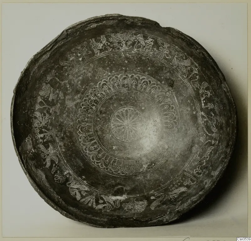 Shallow dark bowl with engraved concentric bands of motifs and a central rosette, photographed from above.