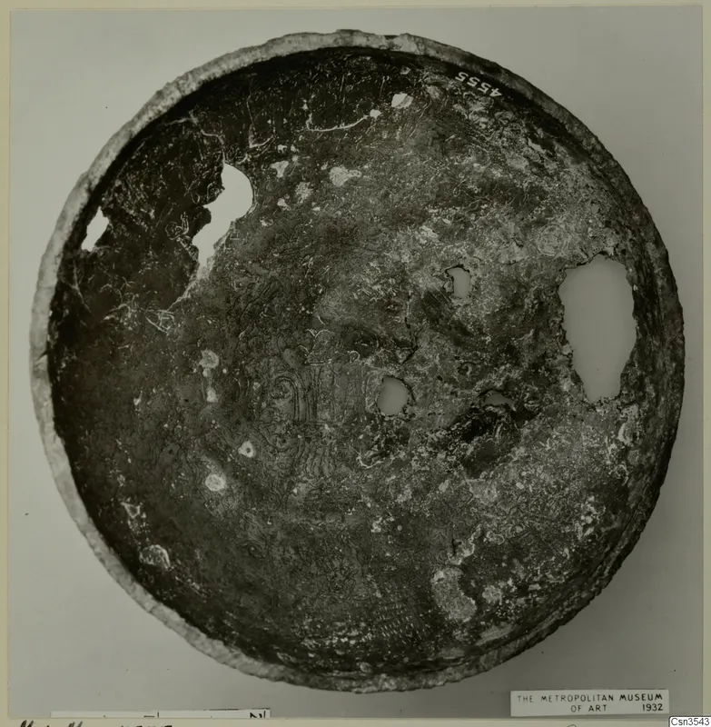 Corroded bowl seen from above, with holes in its surface and incised figures and patterns in the centre