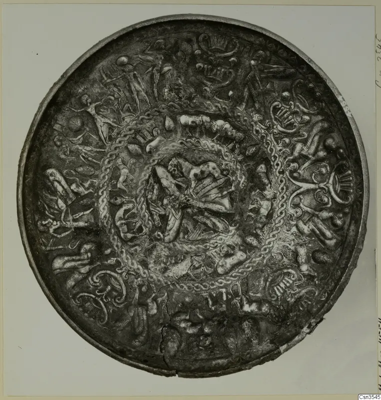 Round metal bowl with raised figures, animal shapes and twisted bands in concentric zones, photographed on a pale card.