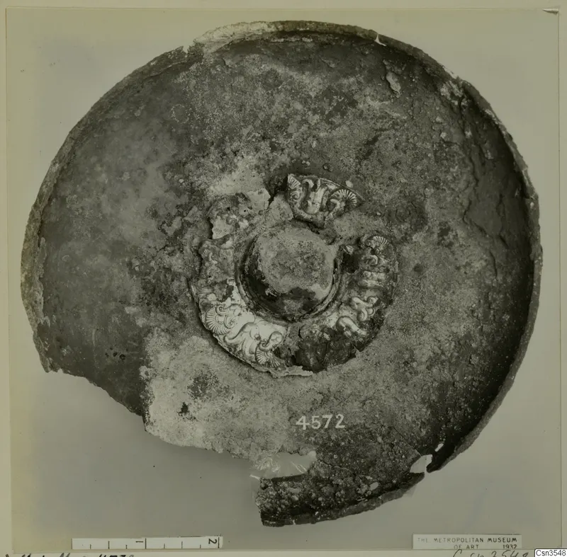 Shallow round vessel seen from above, with a raised central boss ringed by pale scroll-like relief ornament