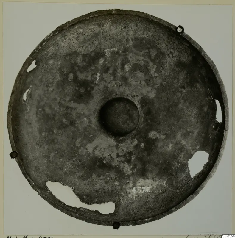 Shallow circular metal dish with a central boss, photographed from above on a mount card